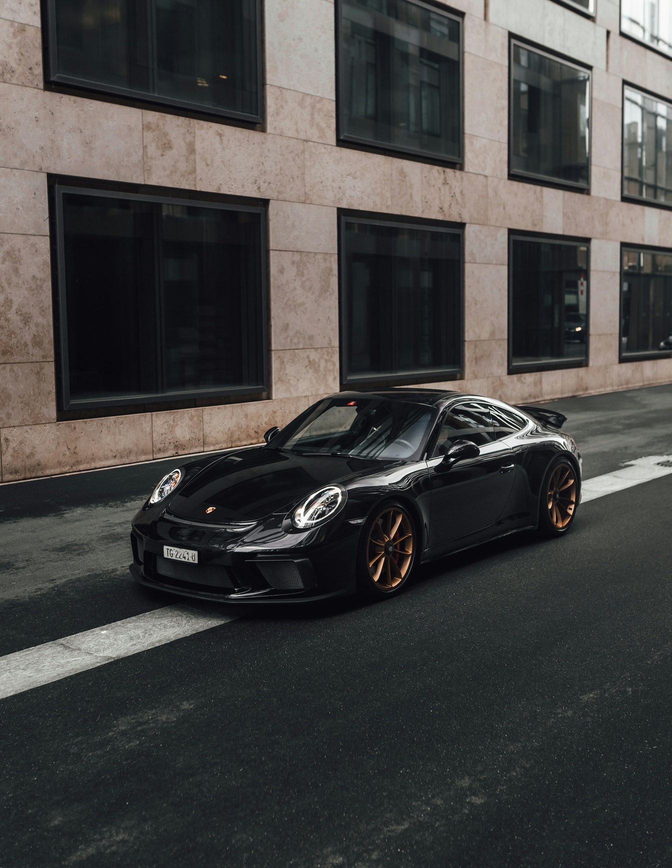 A custom Branders Porsche 911 Carrera Turbo with a carbon fiber hood and vents, lightly covered in raindrops, parked on a wet surface.