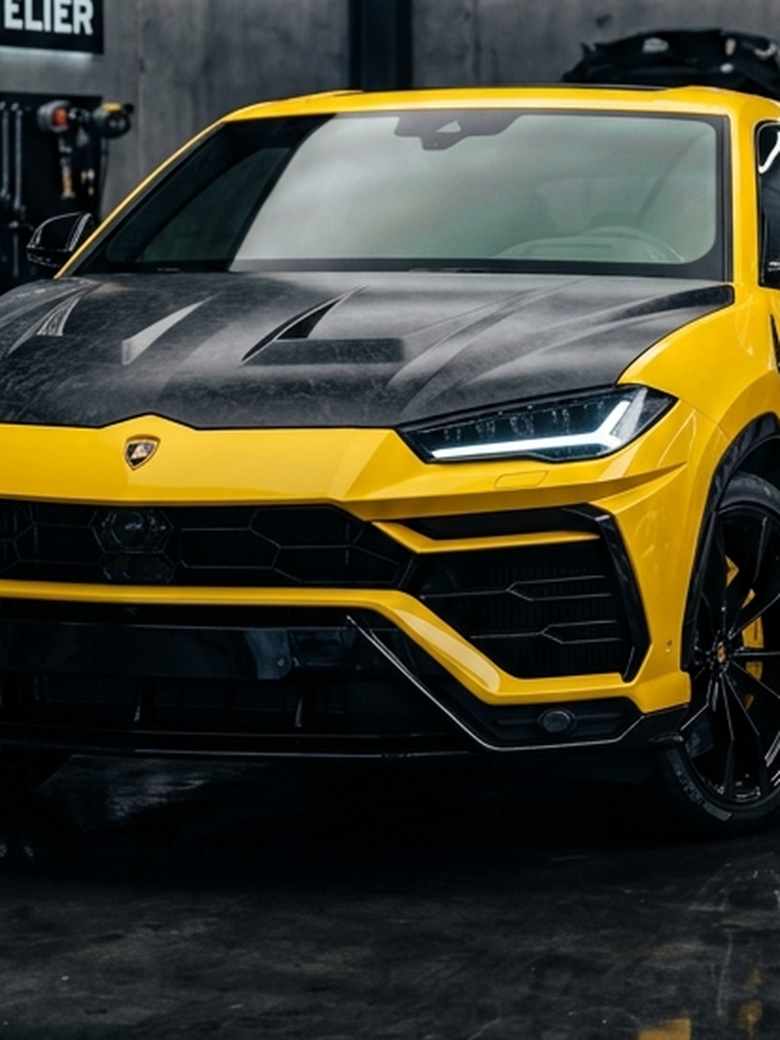 A custom Branders Lamborghini Urus parked on a workshop floor, focusing on its forged carbon hood and yellow front fascia.