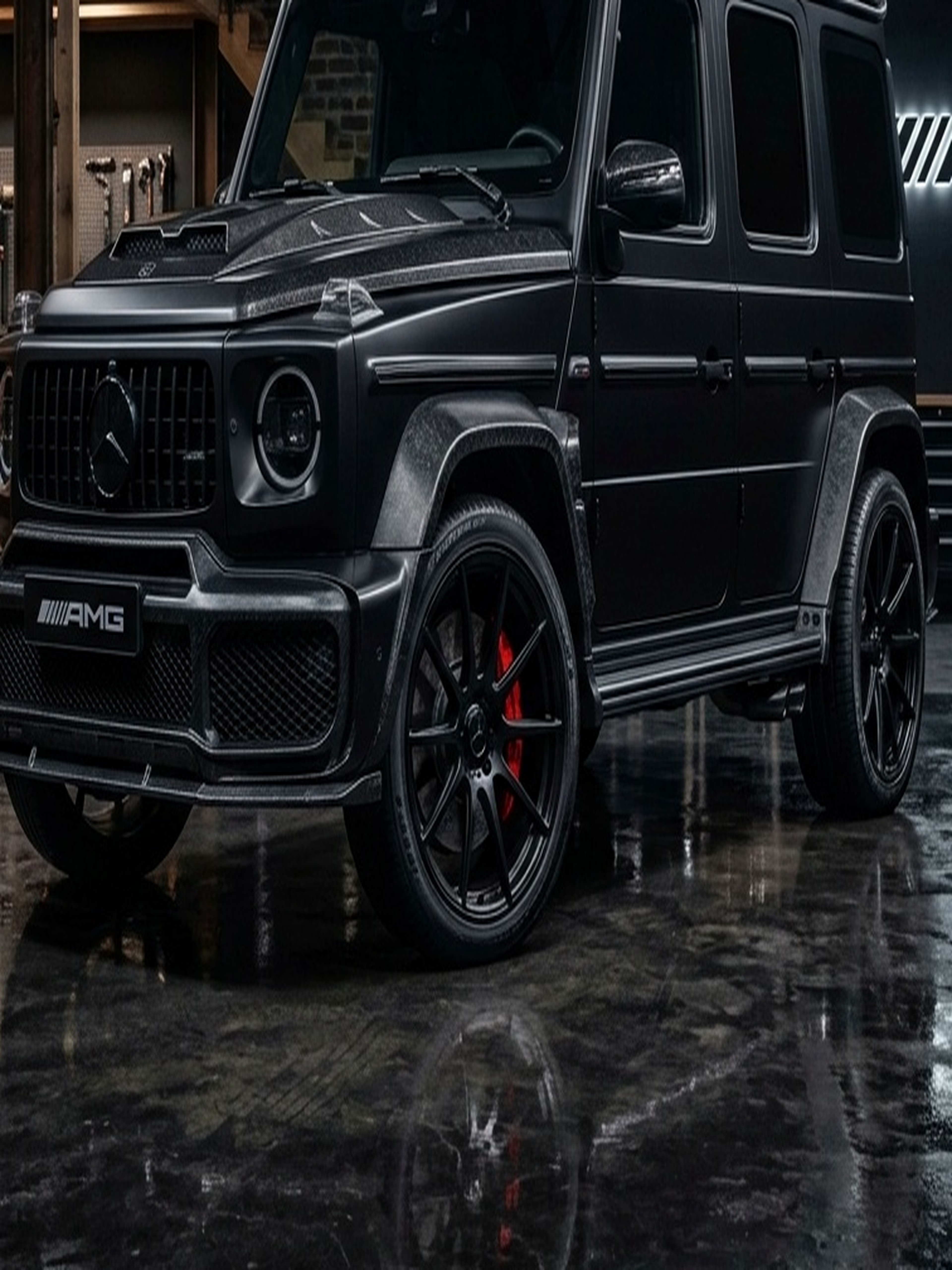 A custom Branders Mercedes G63 in dark green is parked on a wet concrete lot in front of a modern gray building with large windows.