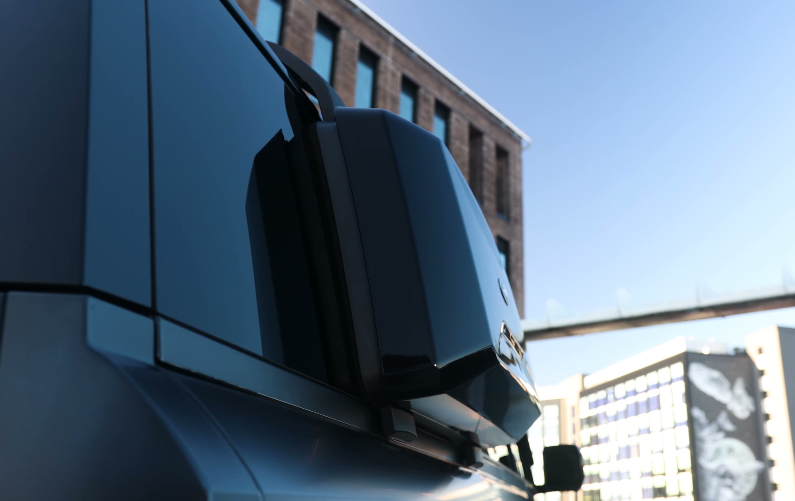 A custom Branders Land Rover Defender 130, matte black, is parked on a concrete rooftop with a brick building in the background.