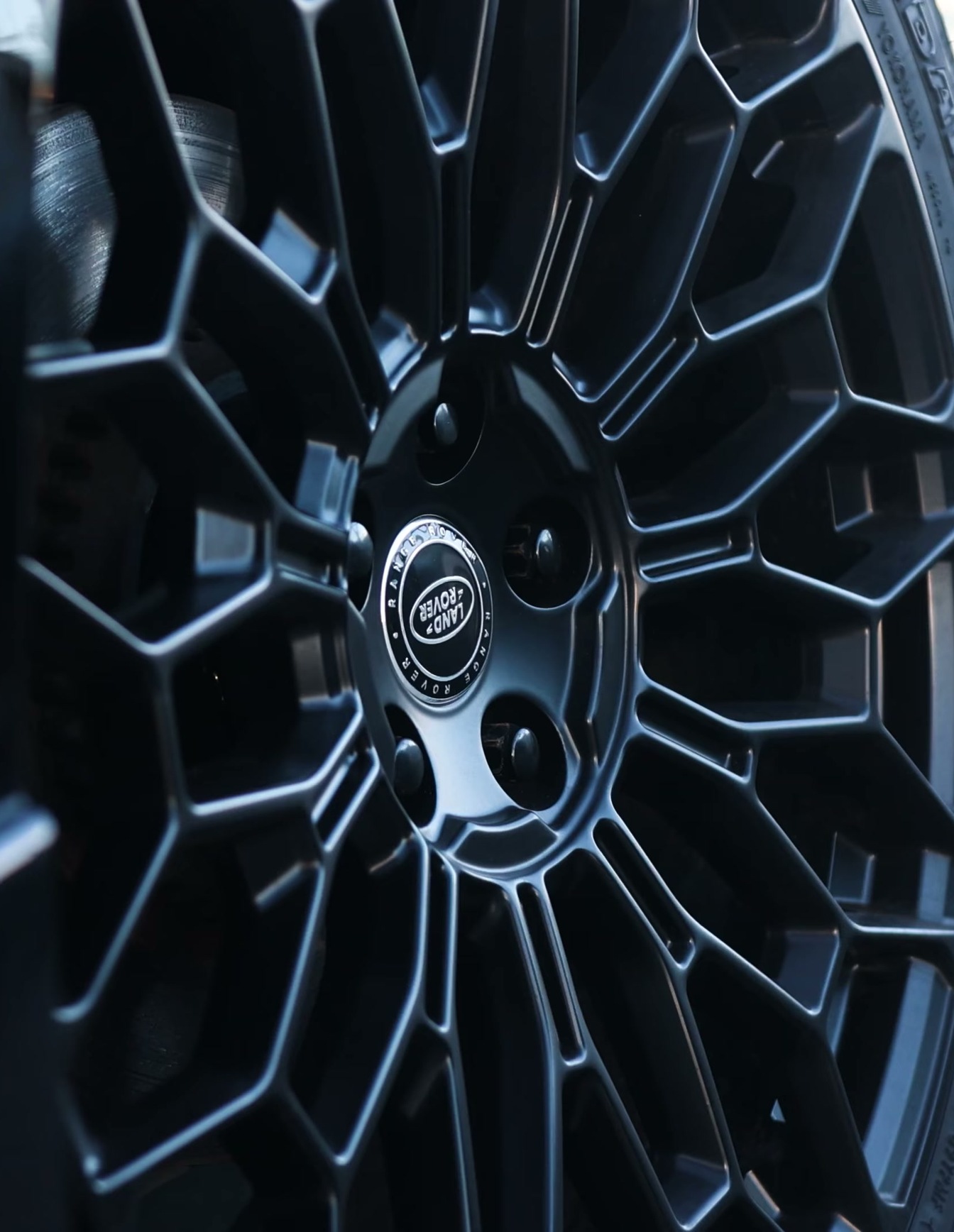 A custom Branders Land Rover Defender 130 wheel with a black geometric spoke design and a Yokohama tire is parked on asphalt.