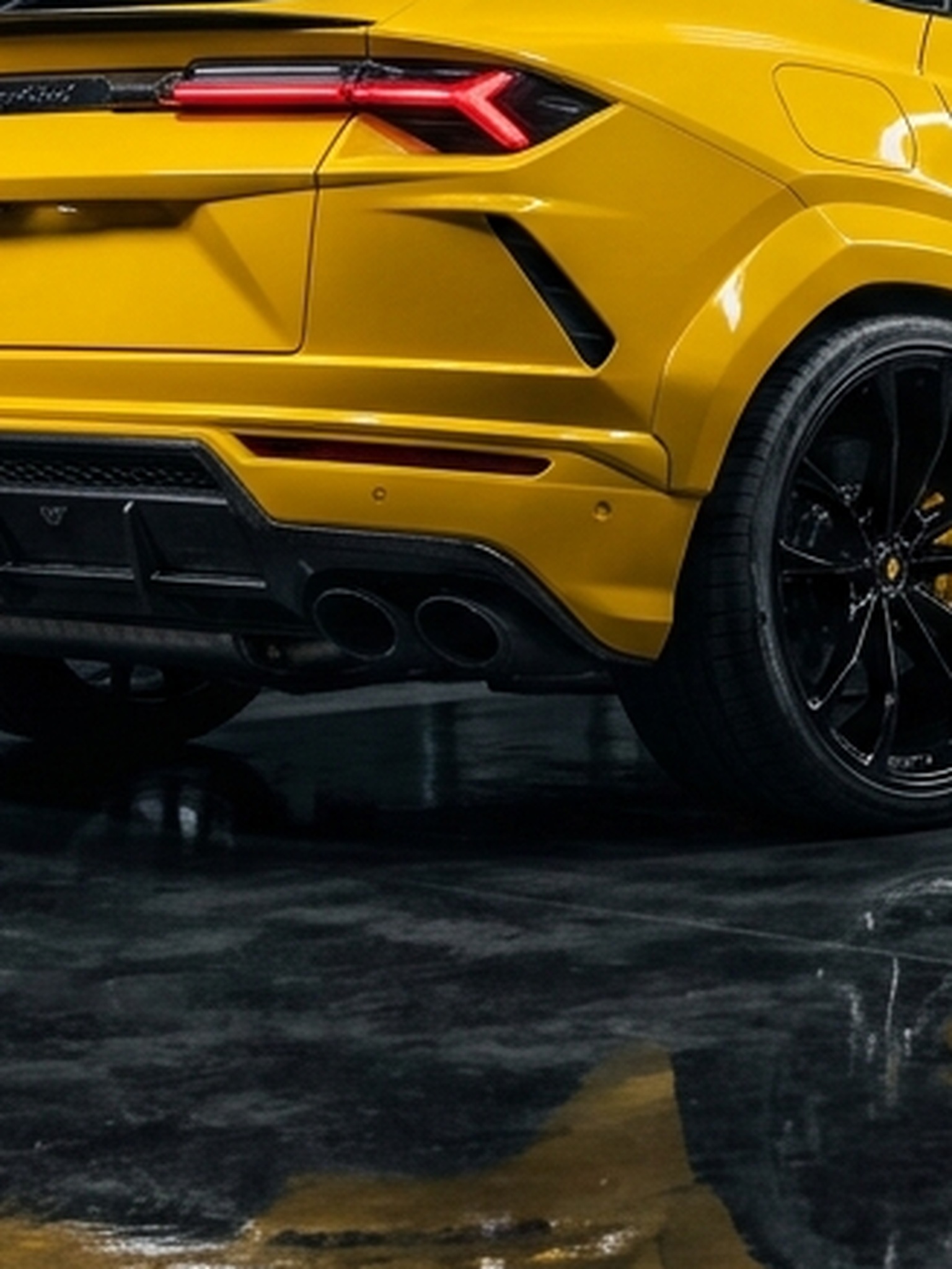A close-up of the forged carbon fiber rear diffuser on a yellow custom Branders Lamborghini parked on a tiled workshop floor.