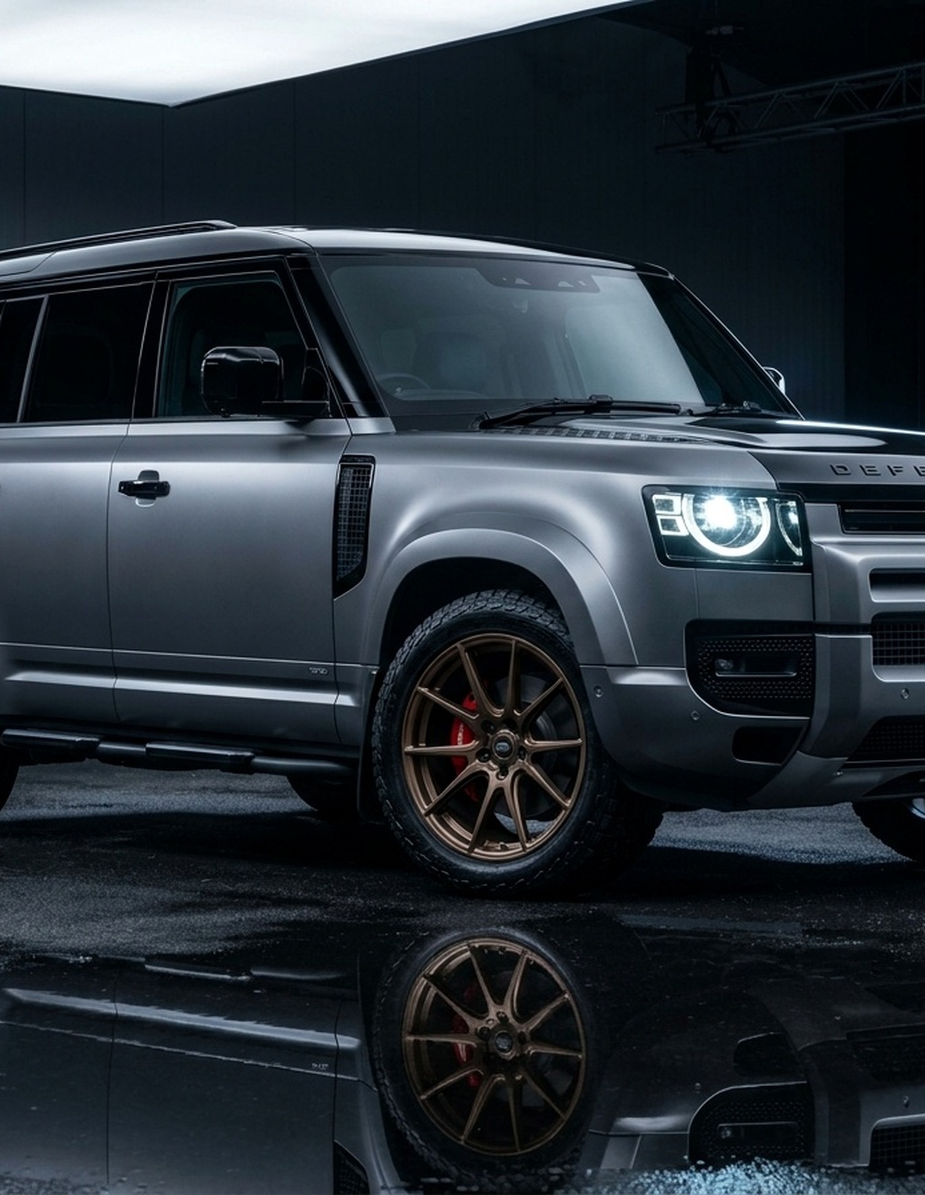 A custom Branders Land Rover Defender 110 with a matte gray finish and glossy black fender flares is parked indoors.