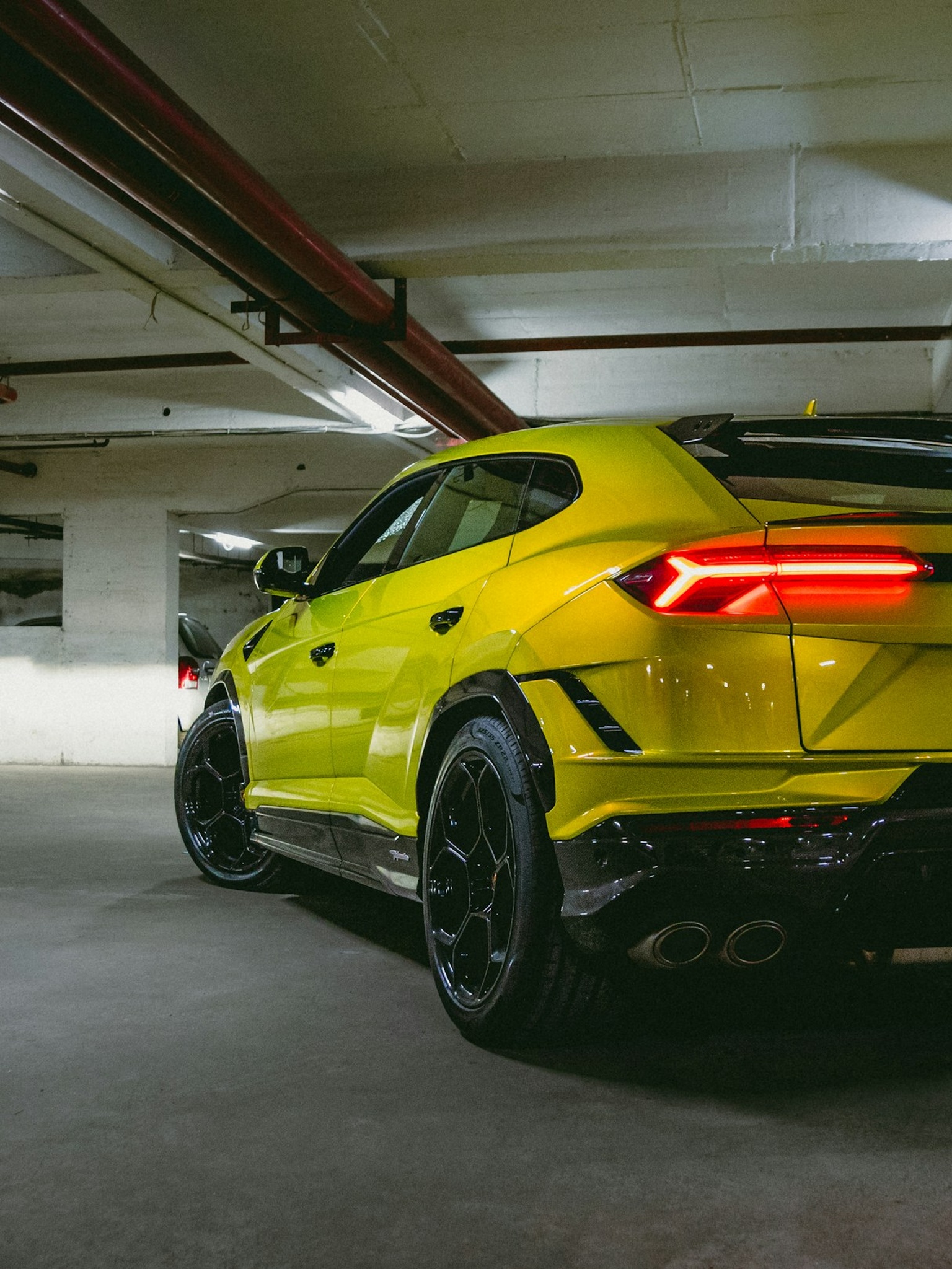 A bright yellow custom Branders Lamborghini Urus parked inside a workshop with patterned black flooring and white brick walls.