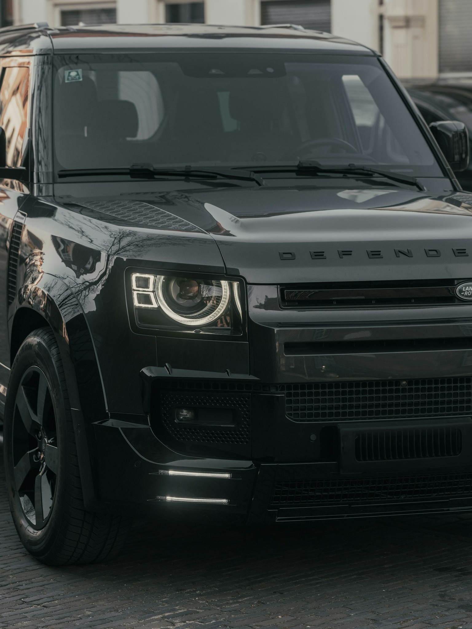 A close-up of a custom Branders Land Rover Defender 90 parked on a roadside with its headlights illuminated.