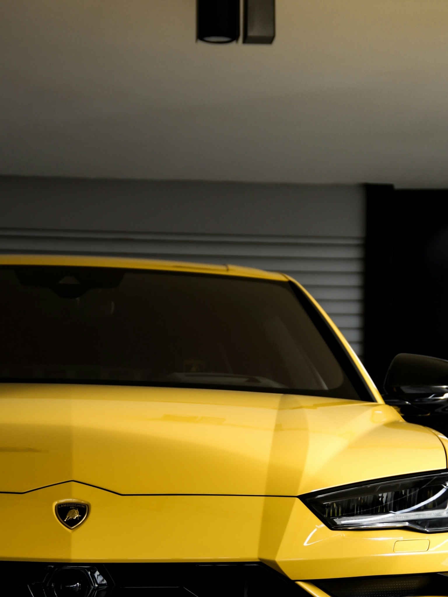 A close-up view shows the yellow front bumper and grille of a custom Branders Lamborghini Urus parked inside a workshop