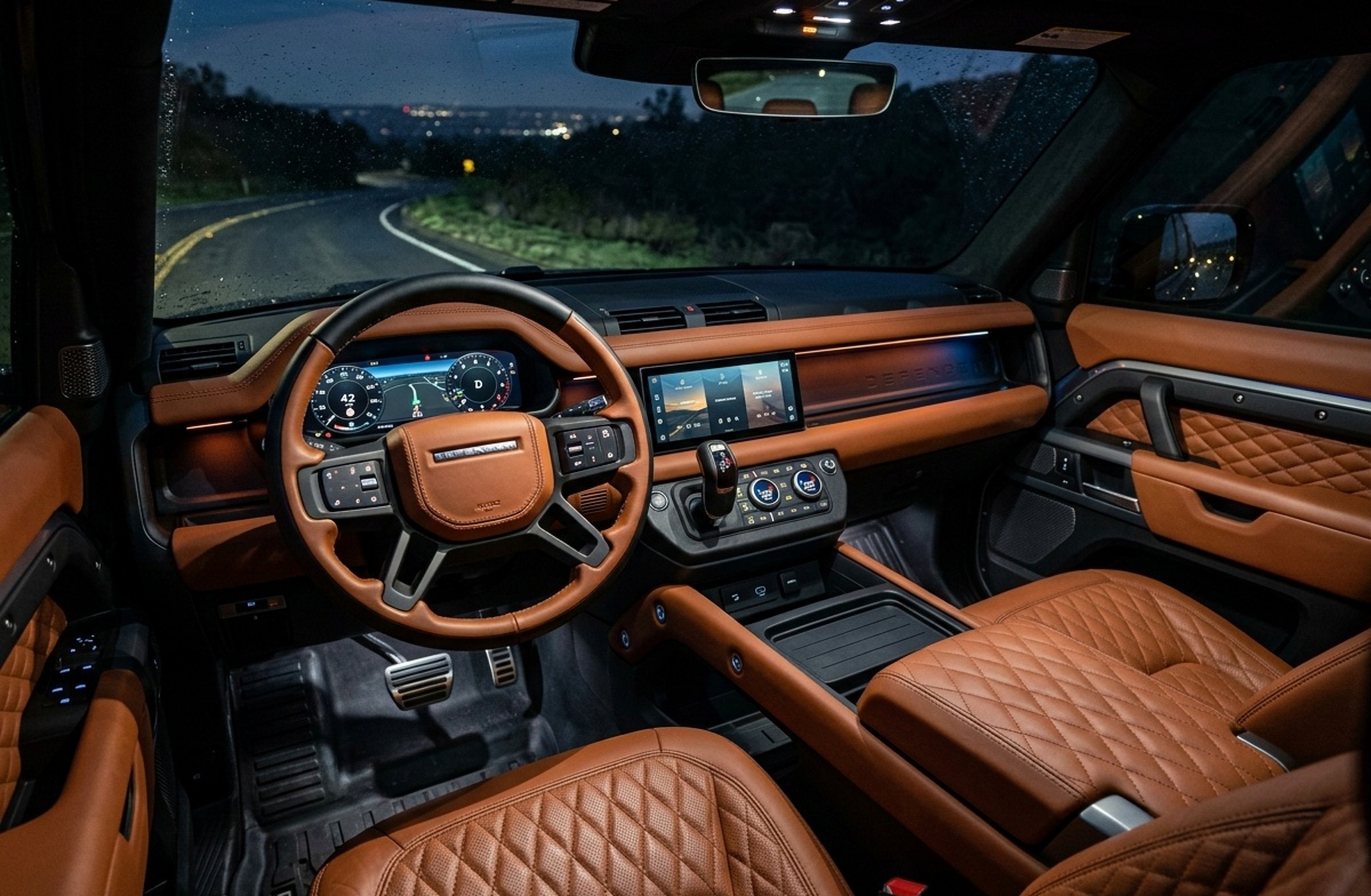 A custom Branders Land Rover Defender 110's running boards and tire are visible on a wet, dark paved surface.