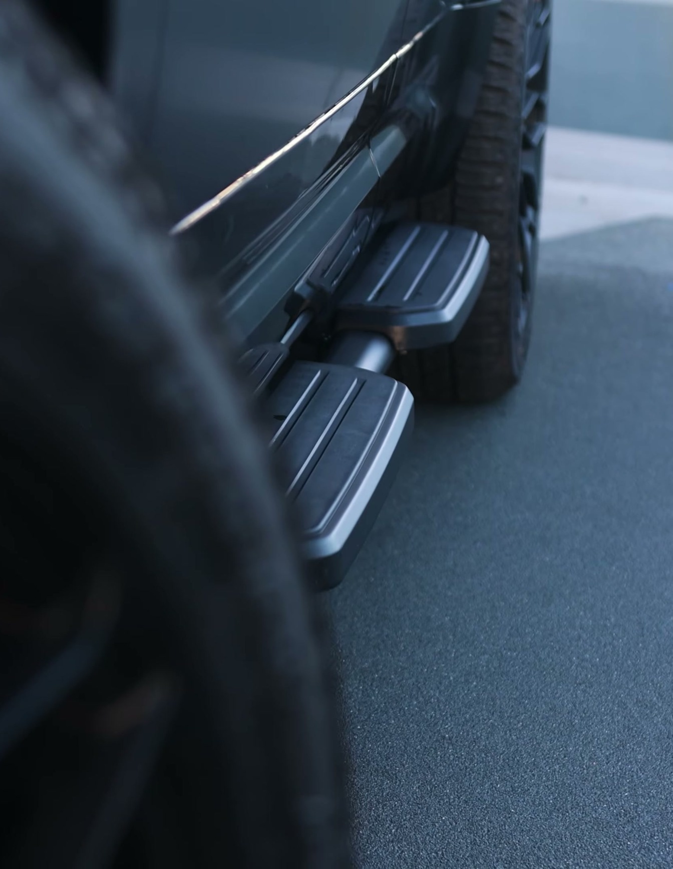 A custom Branders Land Rover Defender 130's black running boards and tire are visible from a low angle on a dark, textured surface.